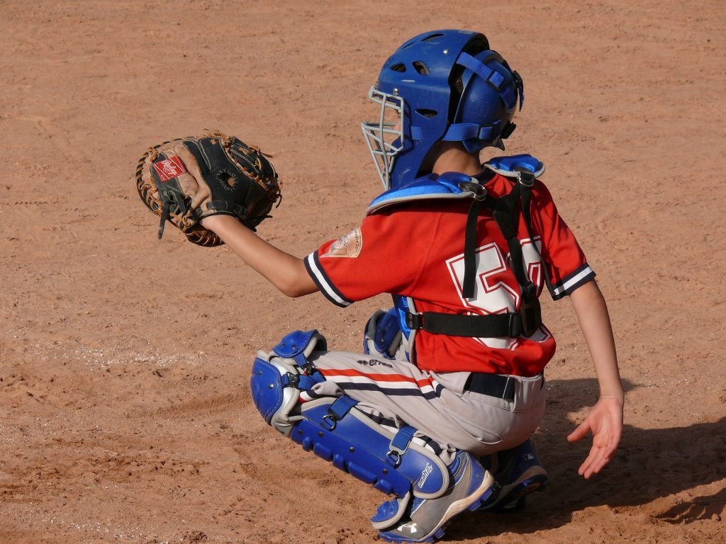 A small child on the playing field wearing catcher's gear. His statue is upright and it seems like he was taught about sportsmanship. 